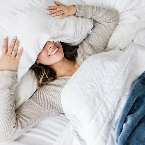 Woman in bed looking happy resting with pillow over her eyes